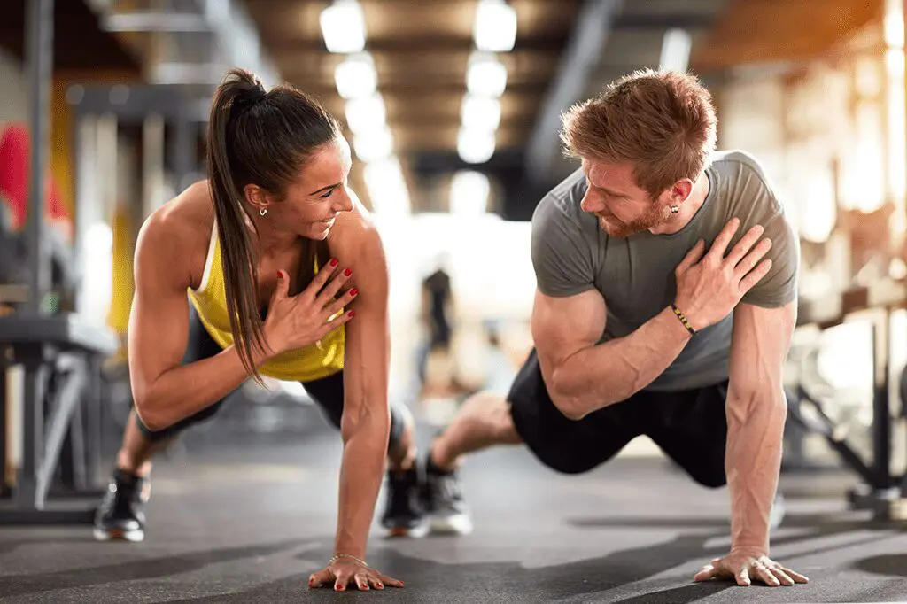 A man and woman doing push ups in the gym.