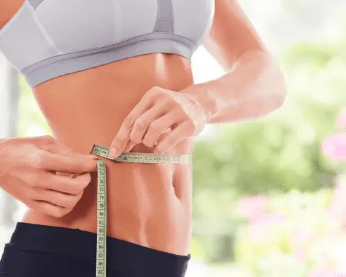 A woman is measuring her waist with a tape measure.