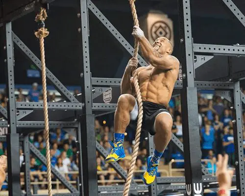 A man is climbing up a rope in front of an audience.