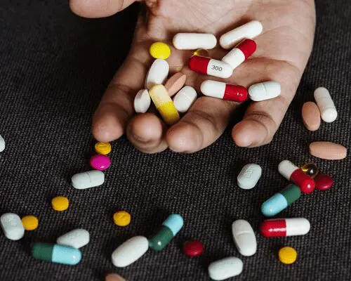 A person holding pills in their hands and scattered on the ground.