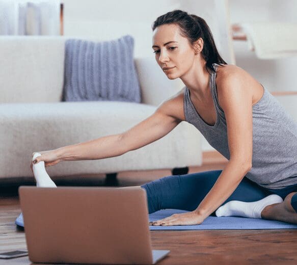 A woman stretching on the floor in front of a laptop.