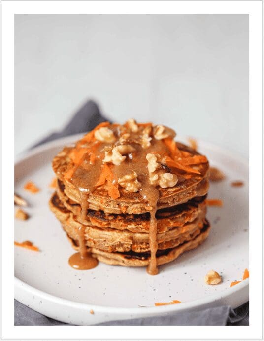 A stack of pancakes with nuts and caramel sauce.