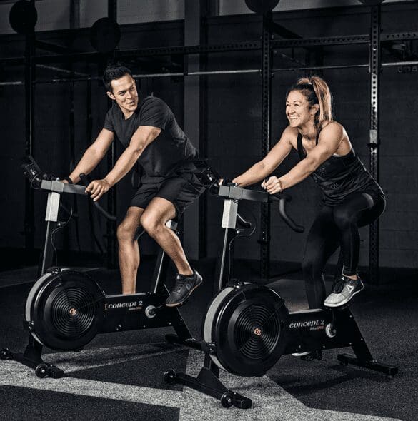 Two people are riding stationary bikes in a gym.