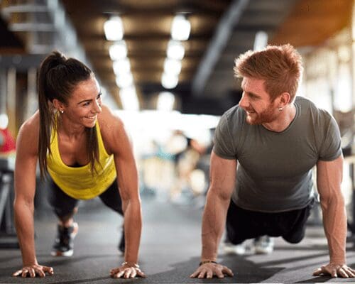 A man and woman doing push ups in the gym.